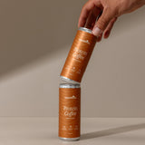 Two cans of Protein Coffee being held against a beige background