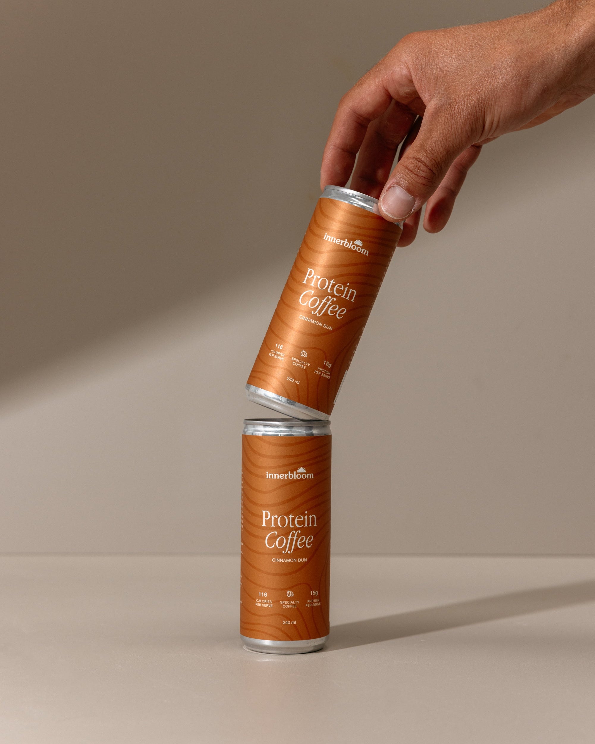 Two cans of Protein Coffee being held against a beige background