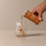 Hand pouring Protein Coffee from a can into a glass on a beige background