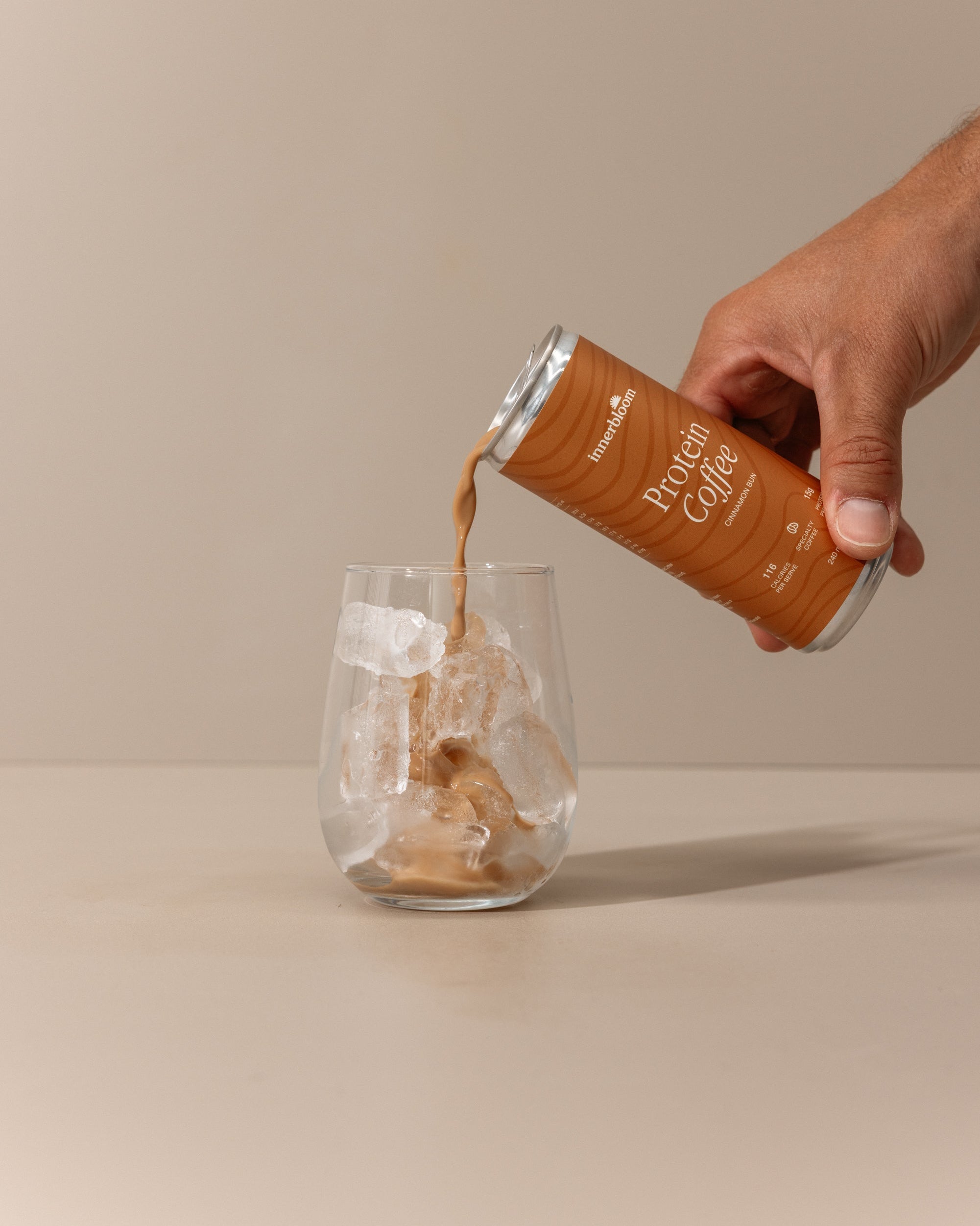 Hand pouring Protein Coffee from a can into a glass on a beige background