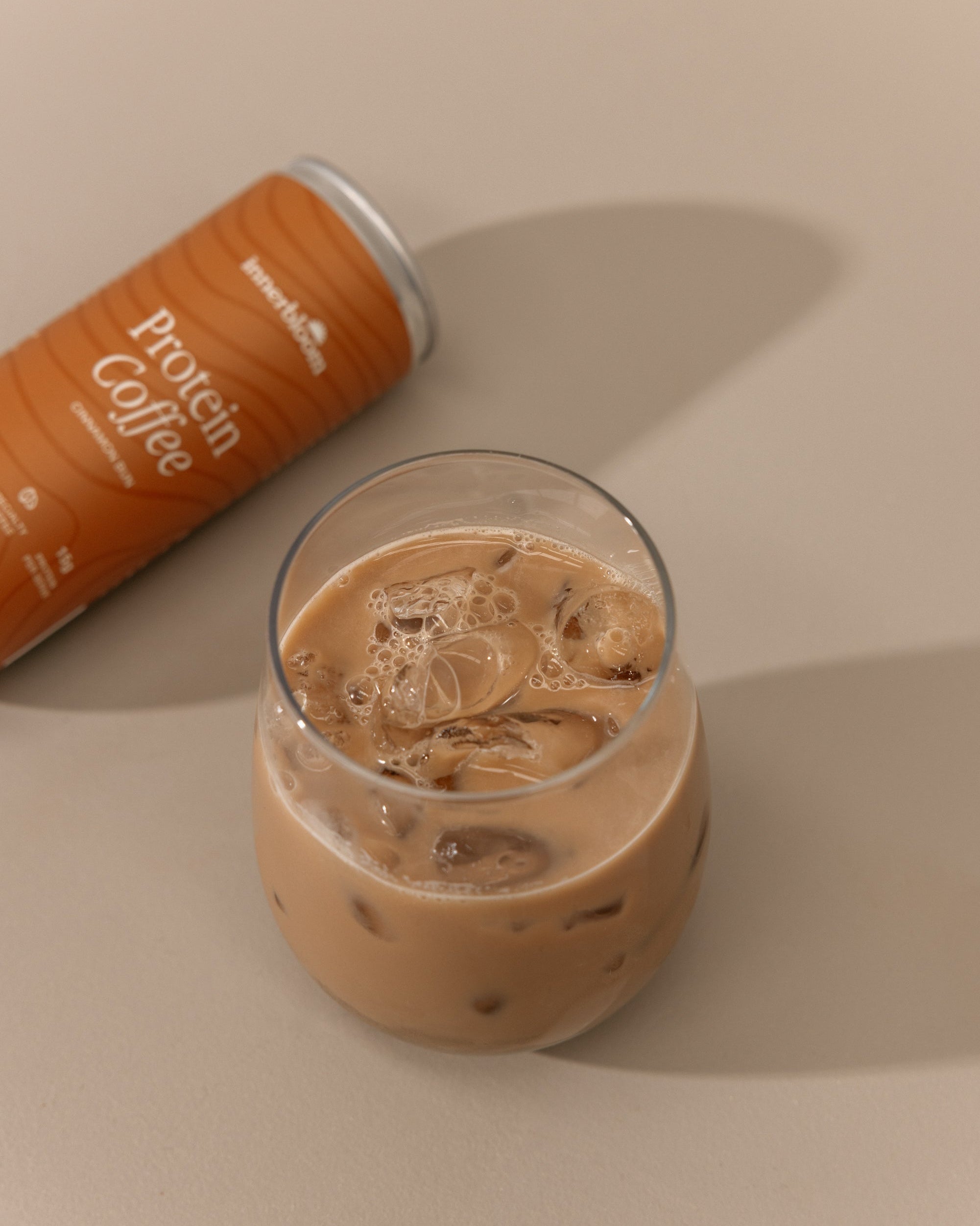 Glass of iced coffee with a can of Protein Coffee on a beige background